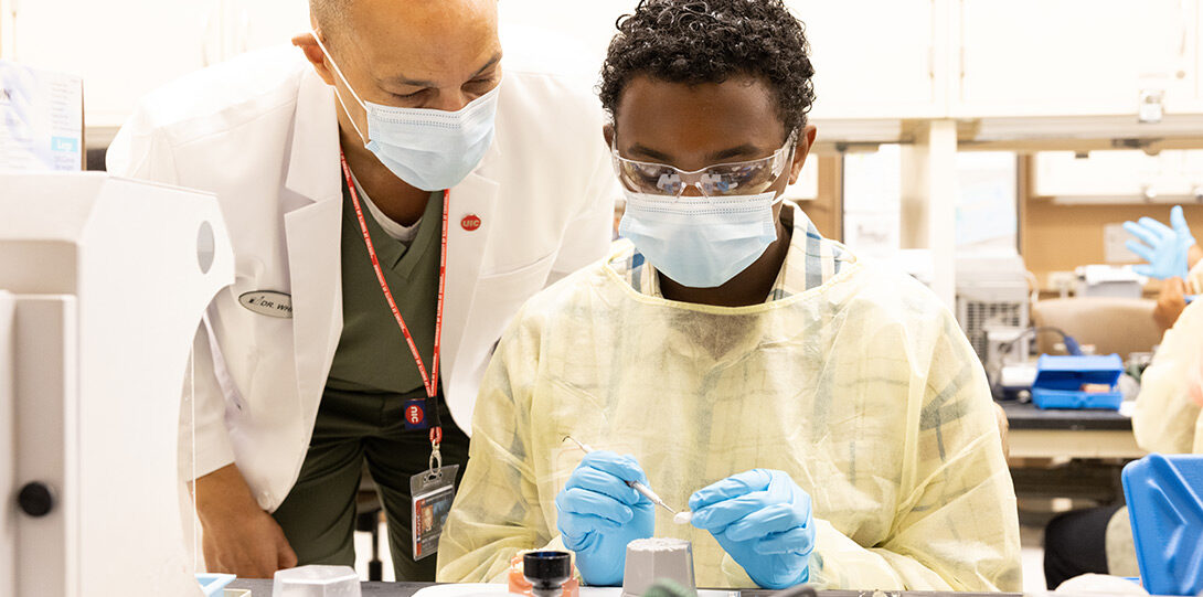 A young Black man being guided by a Black male professor in dental techniques