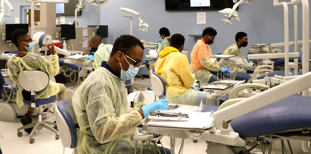 photo of several young Black men in masks and gowns engaging in experiential learning about dentistry