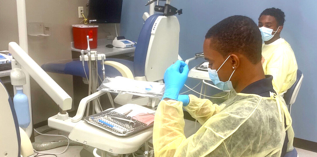 closeup of two young Black men in masks and gowns engaging in experiential learning about dentistry