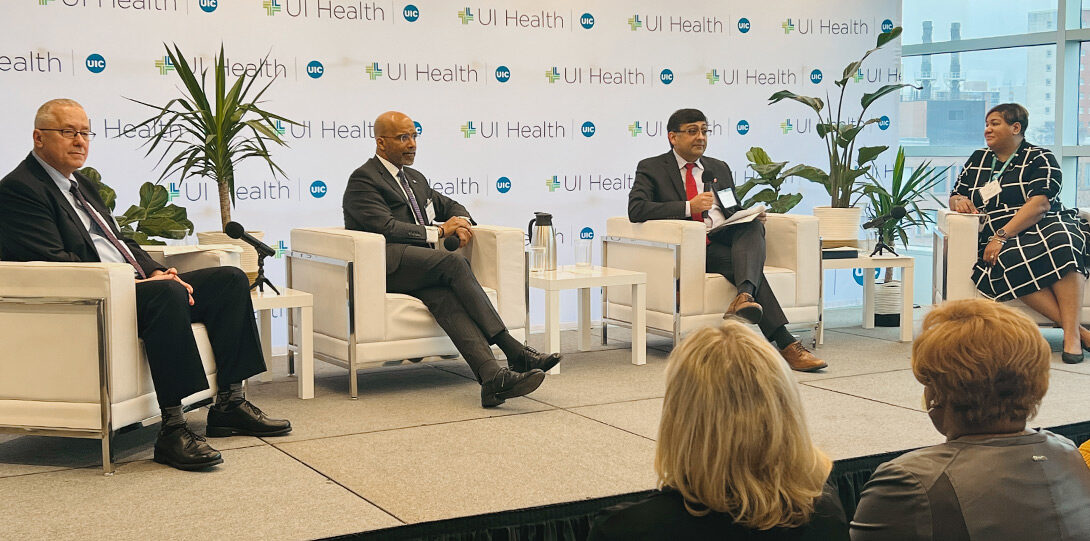 the four panelists sitting in large white chairs on a stage, against a UI Health-themed backdrop