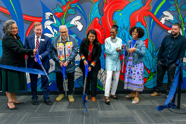 UIC leadership and other key stakeholder lined up in front of the mural and cutting a large blue ribbon with large scissors