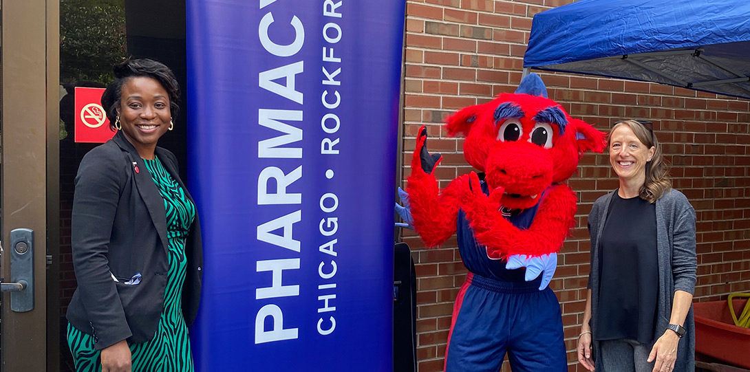the two named people and Spark D. Dragon standing next to a banner that says UIC Pharmacy, Chicago, Rockford