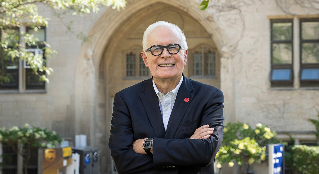 Dr. Irwin standing smiling, with arms folded, withe the College of Medicine in the background