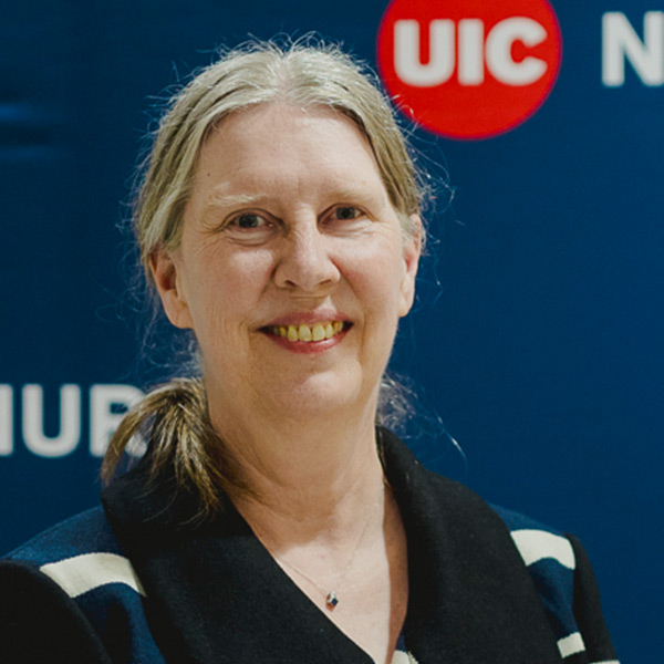 women with blonde hair, puled back in a pony tail, smiling and standing in front of a UIC Nursing-themed backdrop