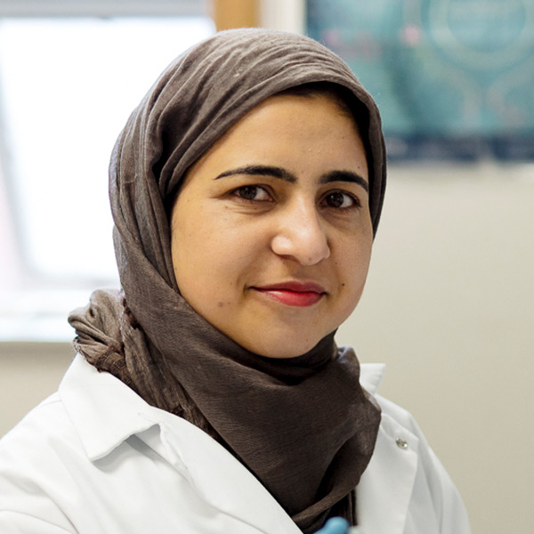 woman wearing a dark-colored hijab and a white lab coat, posing in a laboratory