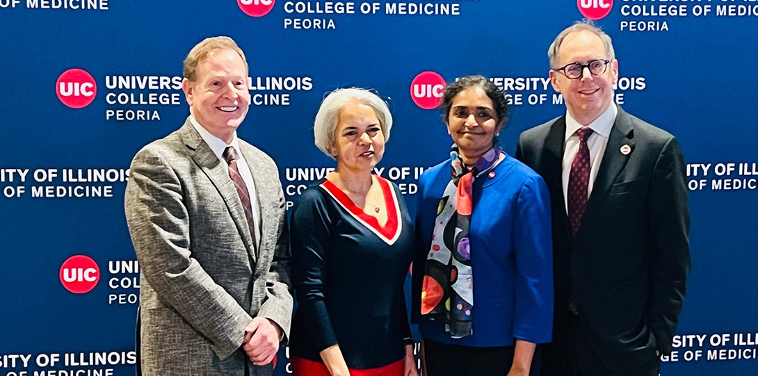 The named individuals wearing formal attire and posing together in front of a background with repeating logos for the University of Illinois College of Medicine Peoria