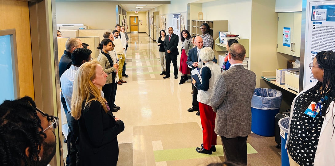 looking down a hallway in a laboratory, with various people standing on either side of the hallway listening as someone talks about the lab