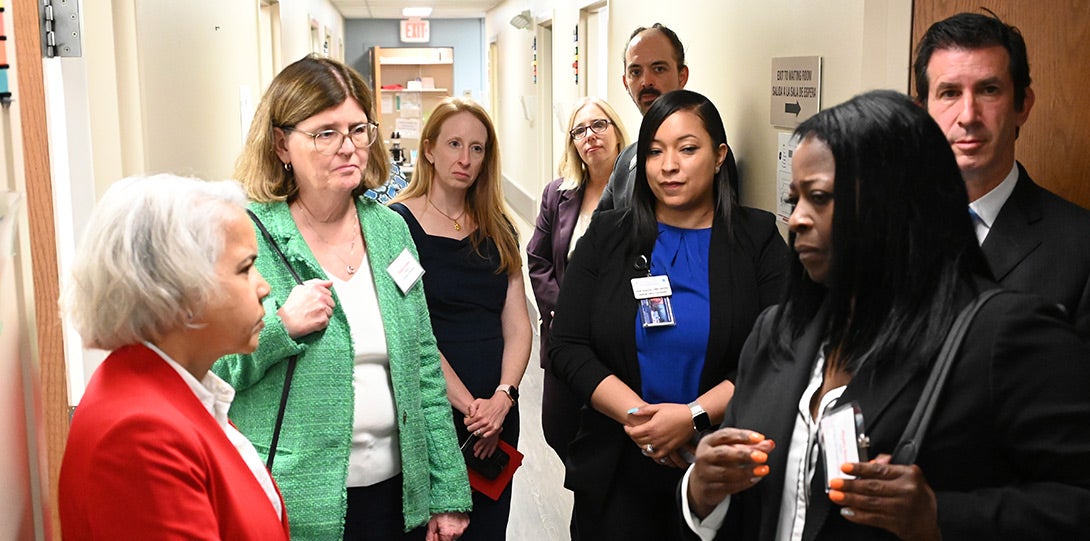 at left, the chancellor in a red jacket and a woman in a green jacket and white blouse listening to an African American woman with shjoulder length black hair standing at right and wearing a black jacket and white blouse