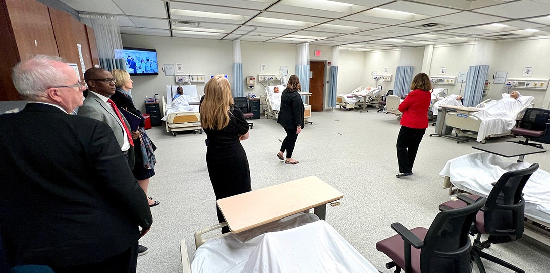 a wide shot of the various tour attendees in a large simulation lab with a number of bays of hospital beds and medical equipment