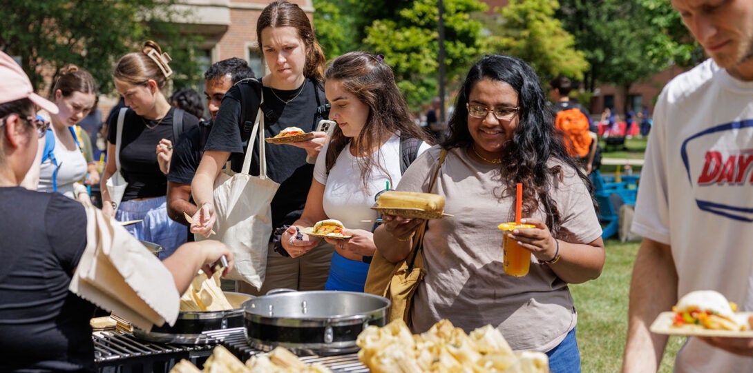 diverse people standing in line at the food tables, getting tamales and bao