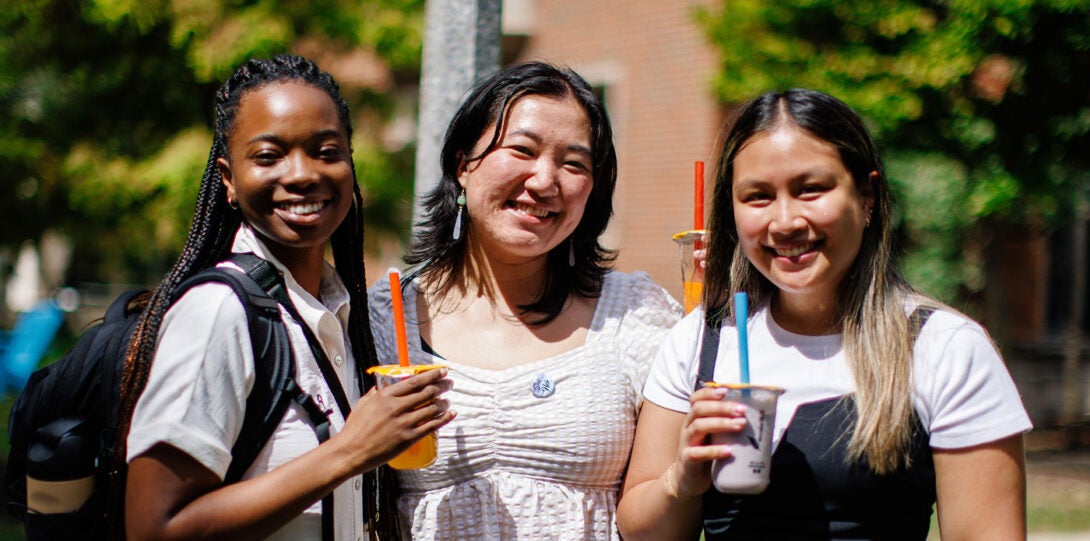 Three young women, one African American, one Asian and one Latinx, smiling and holding cups of boba tea