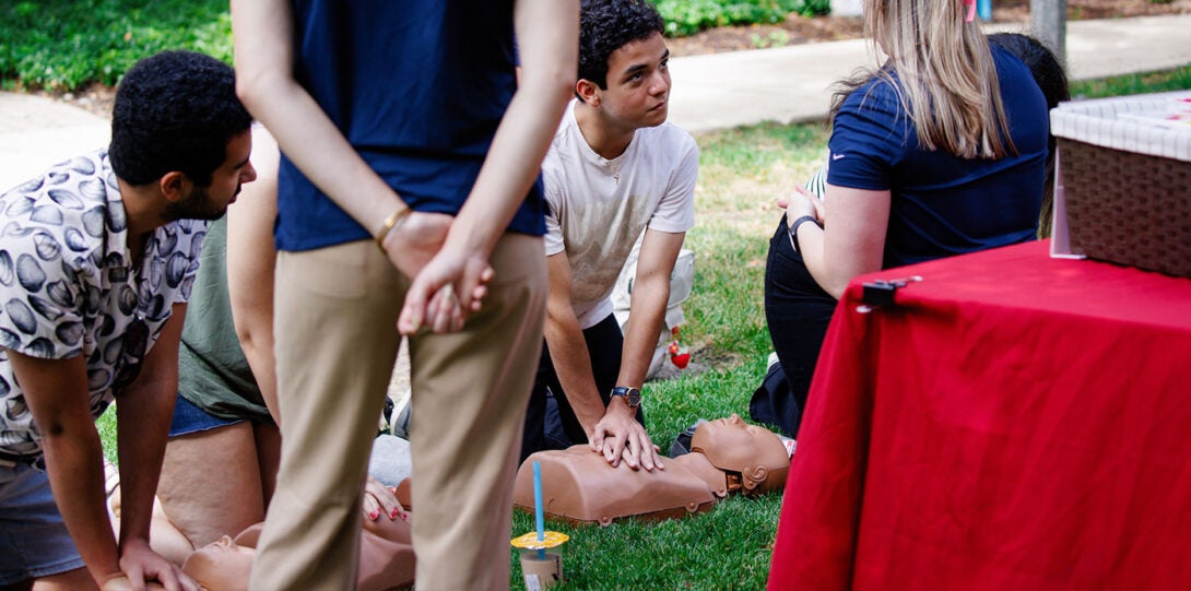 Young people practicing CPR on mannequins that are laying on the grassy lawn