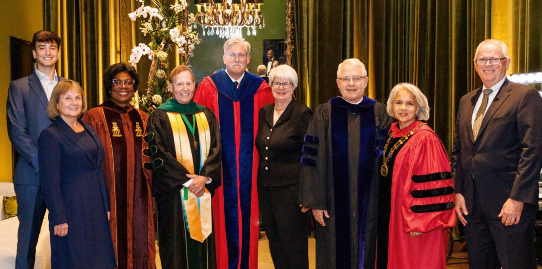 A diverse group of nine people posing together, some in formal attire and some in academic regalia