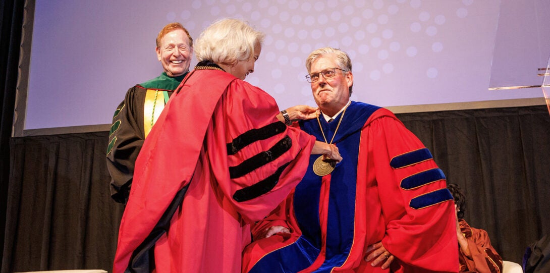 A woman and man wearing red academic regalia, as another man in black regalia looks on.