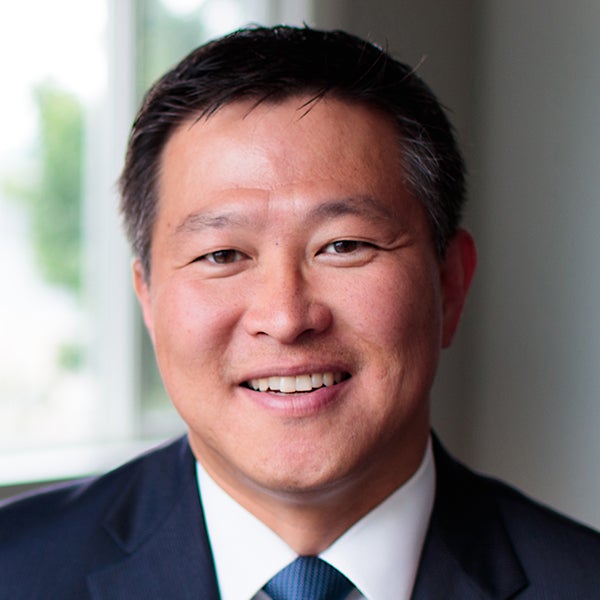 Asian man with short dark hair wearing a dark blue suit jacket, white shirt and blue neck tie